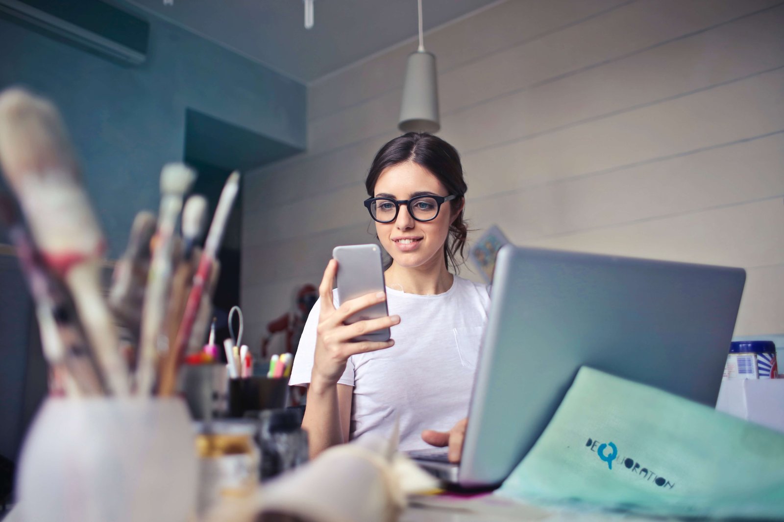 Mujer mirando el celular, trabajando desde la casa en ordenador portatil